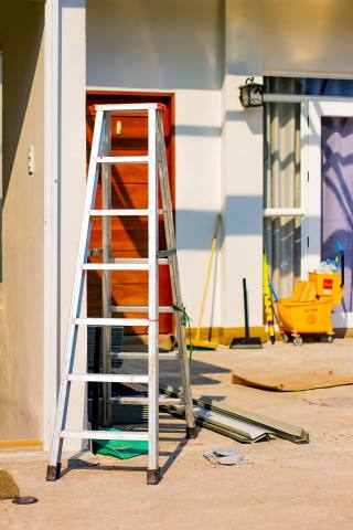 An exterior home renovation area with ladder, tools, and materials.