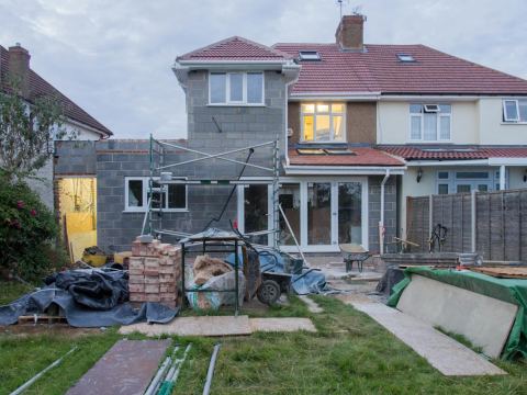 A home addition under construction with scaffolding, materials, and masonry work in progress.