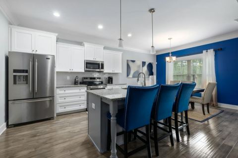 A finished kitchen with white cabinets, blue accents, and a granite island.