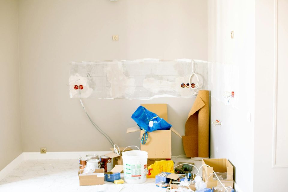 A room under renovation with tools, paint cans, wiring, and repair supplies.